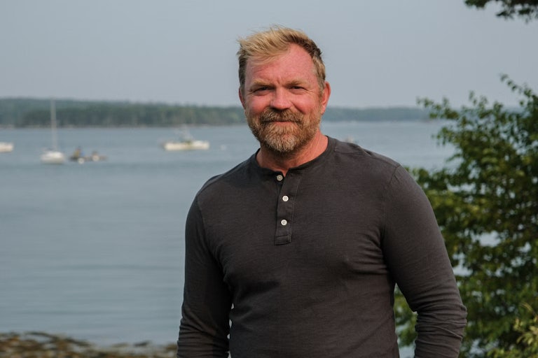 Maine Senate candidate Graham Platner stands in front of a body of water.