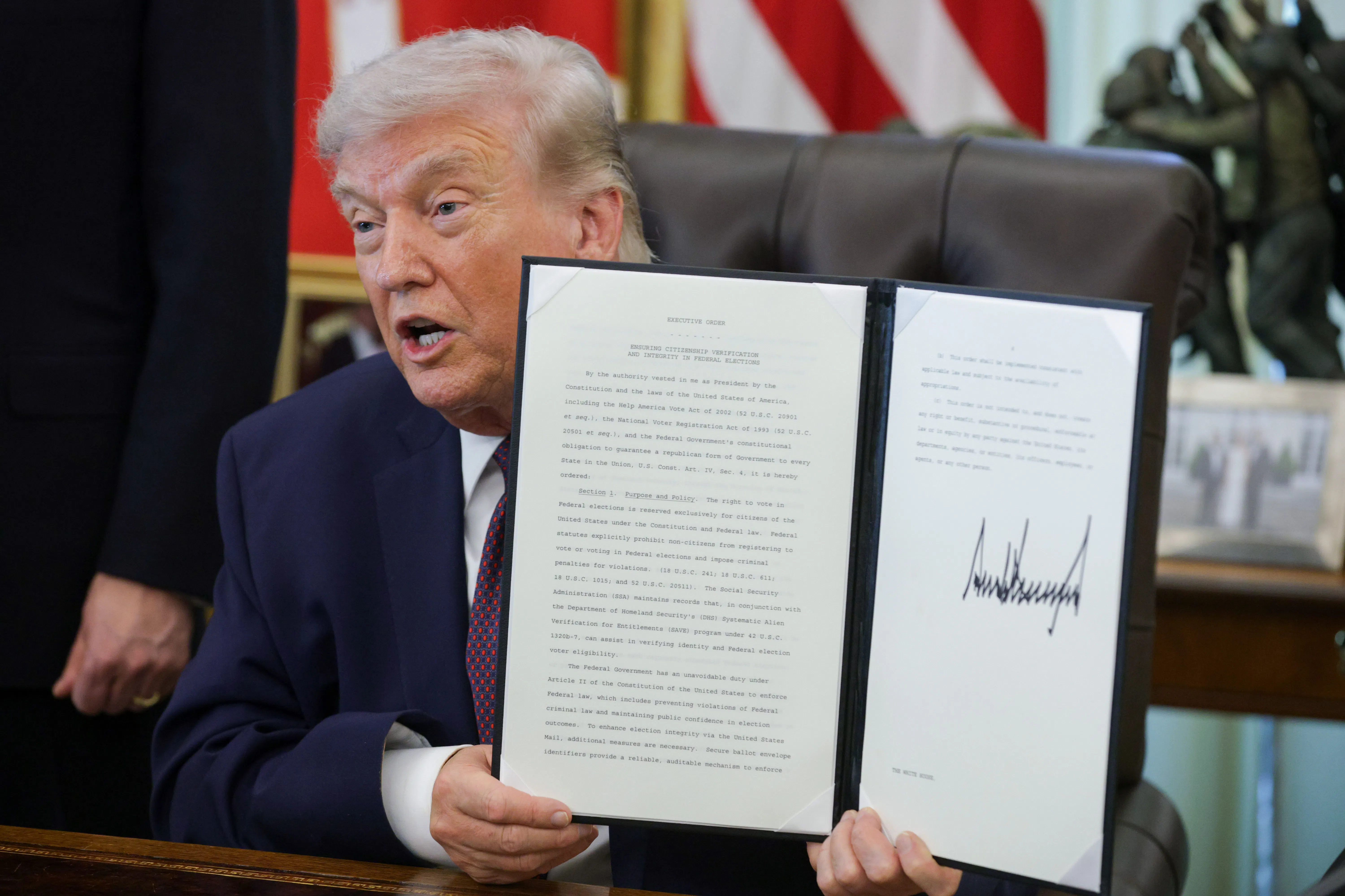 President Donald Trump holds up a signed executive order while sitting at his desk in the Oval Office of the White House.