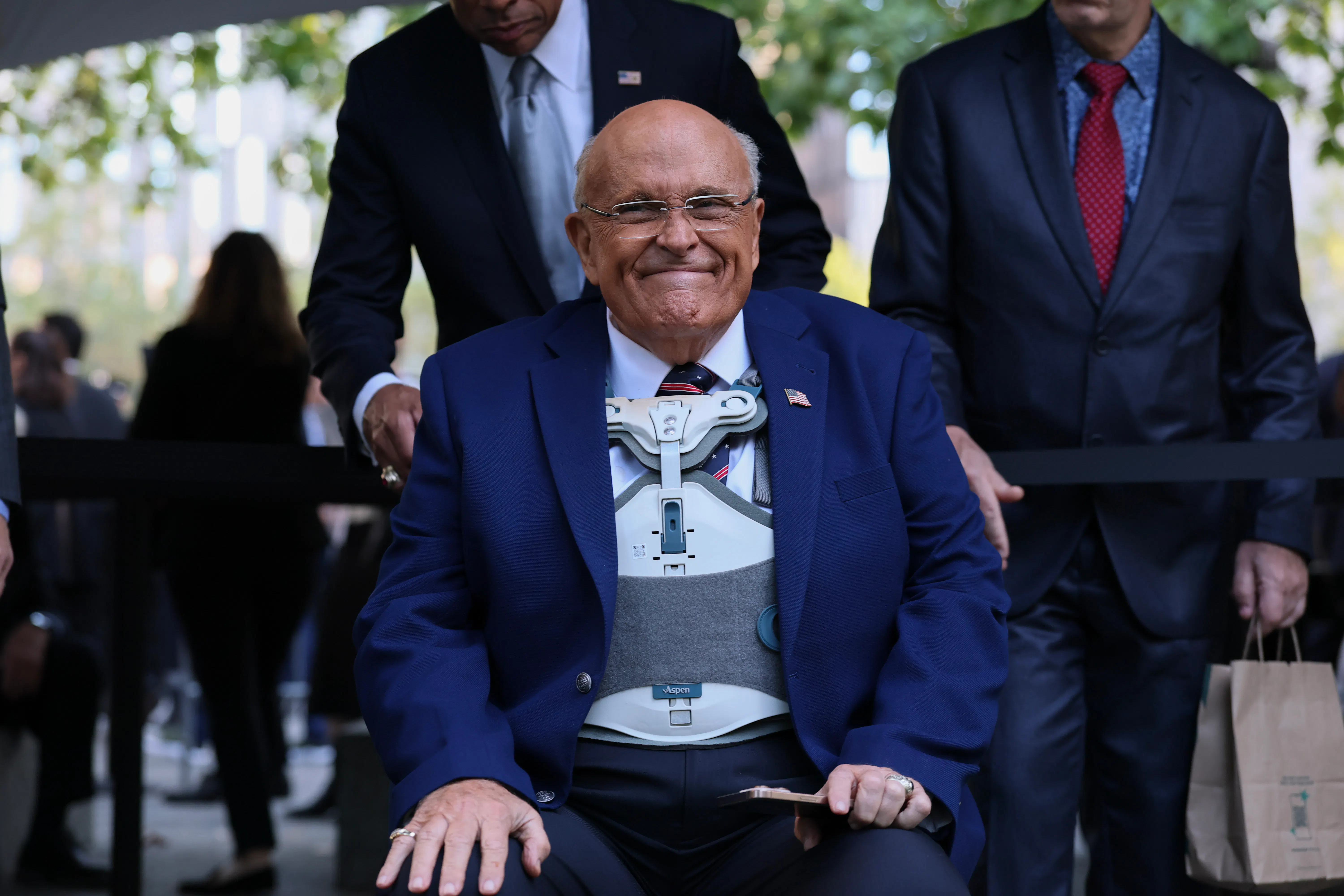 Rudy Giuliani smiles while sitting during a 9/11 memorial ceremony