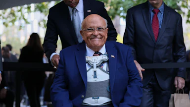 Rudy Giuliani smiles while sitting during a 9/11 memorial ceremony