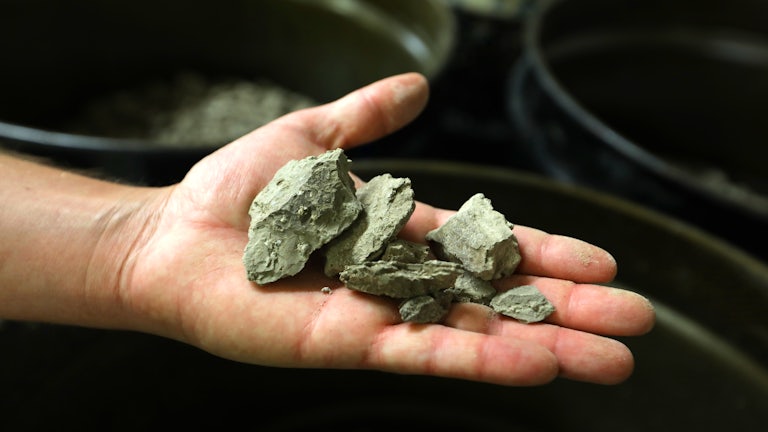 An open hand holds pieces of lithium-rich clay.