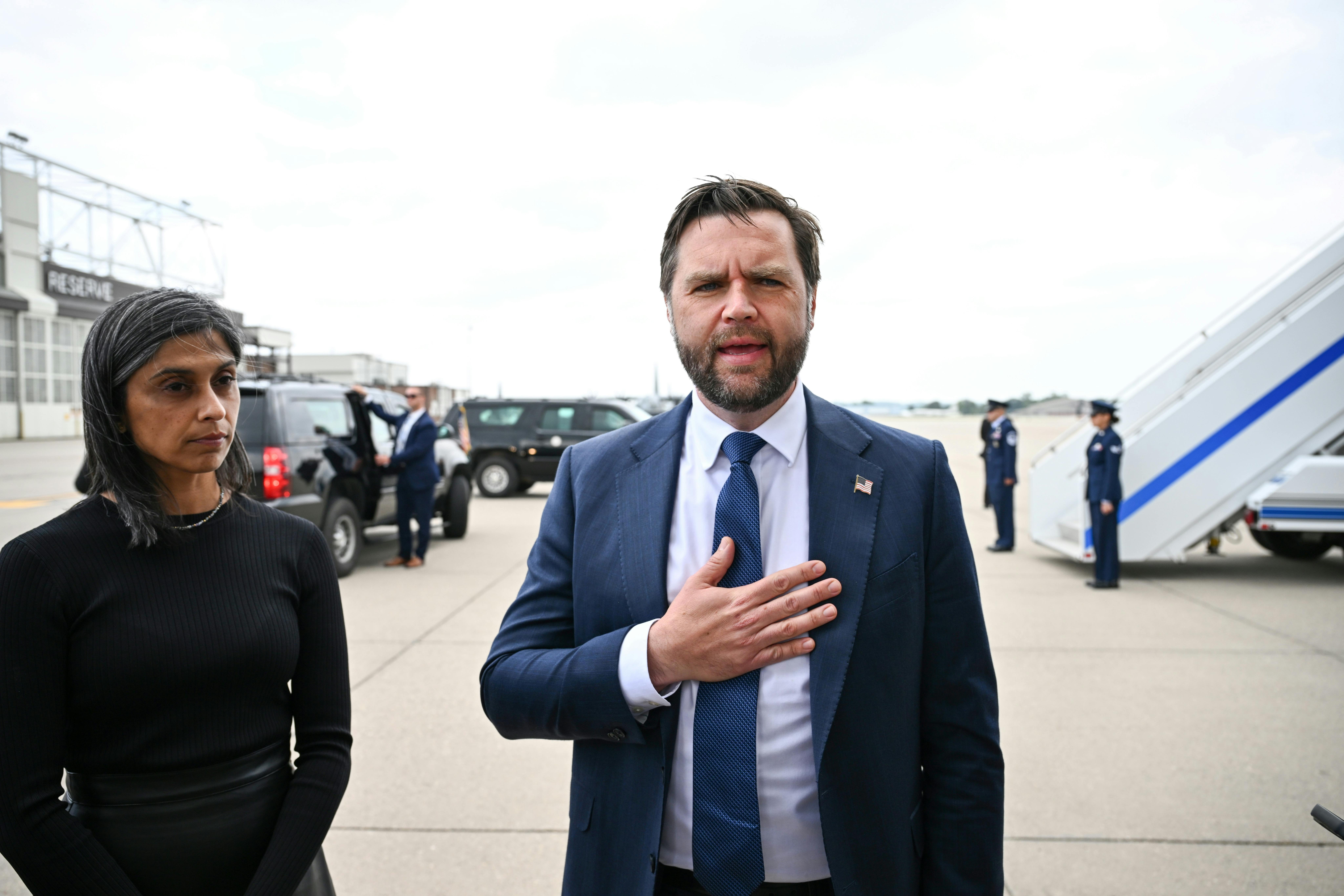 JD Vance speaks with a hand over his chest as his wife Usha zones out. The two are at an airport outside the plane.