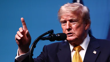 Donald Trump raises a finger while speaking into a microphone.