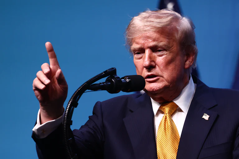 Donald Trump raises a finger while speaking into a microphone.