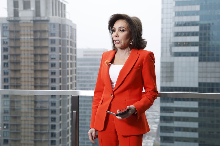 Fox News host Jeanine Pirro standing on a balcony in an highrise building. Two other highrise buildings are seen behind her.