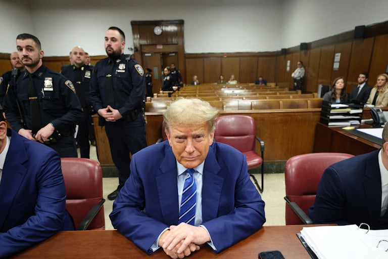 Donald Trump smiles as he sits at a table with his hands folded