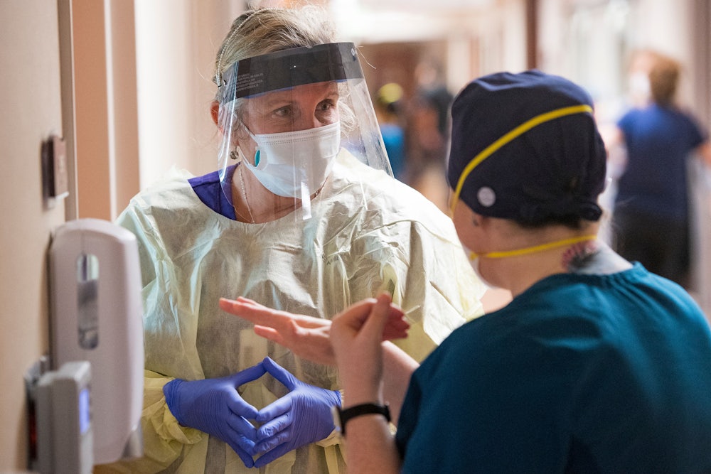a nurse wearing a mask and face shield talks to another nurse in a Covid ICU