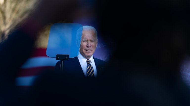 President Biden looks at a teleprompter while addressing a crowd.