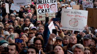 Demonstrators face the camera holding signs reading, among other messages, "Unelected Autocrat" and "Musk Trump Regime Resign!"