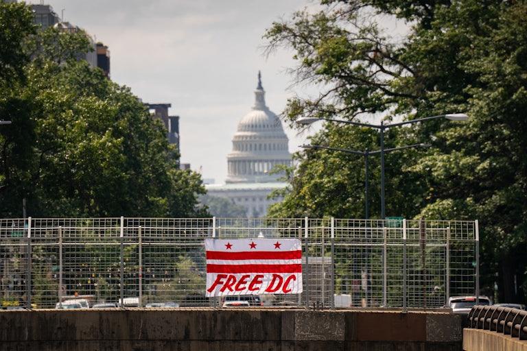 A flag that says, "Free DC" hangs off the side of a bridge. The Capitol is in the background.