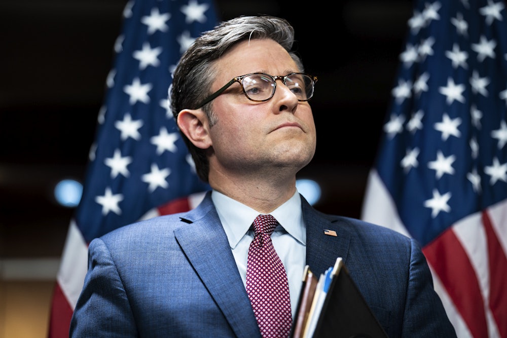 Mike Johnson stands, carrying a folder, with his lips pressed together.