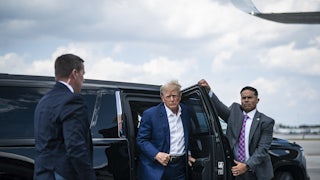 Donald Trump exits a car as someone opens a door for him.