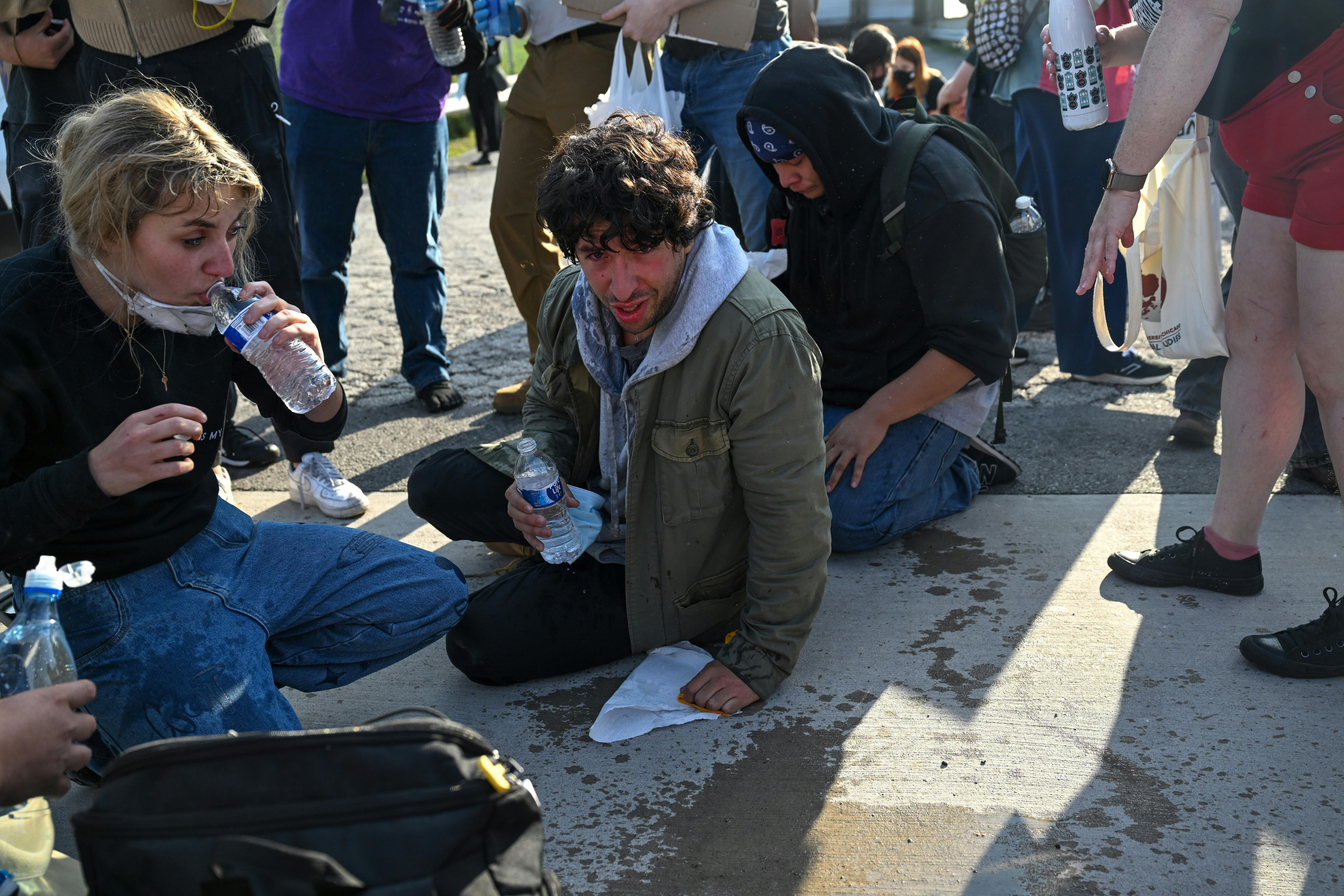 Kat Abughazaleh drinks water while sitting on the ground with others who were tear gassed.