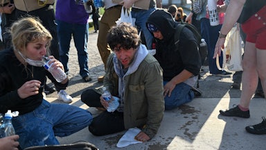 Kat Abughazaleh drinks water while sitting on the ground with others who were tear gassed.