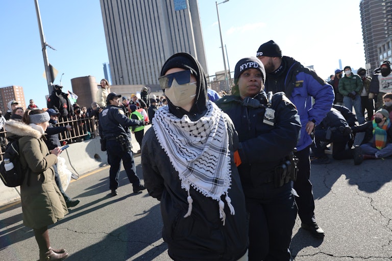 A pro-Palestine protester wearing a keffiyeh and a face mask is arrested by NYPD. Others are in the background