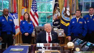 Donald Trump speaks while sitting at his desk in the Oval Office. He is flanked by the astronauts from the Artemis II mission.