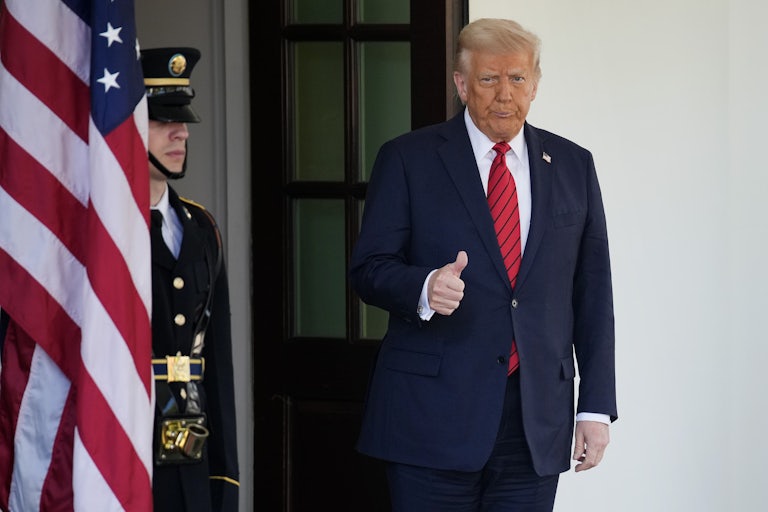 Donald Trump purses his lips and gives a thumbs up standing at the door of the White House
