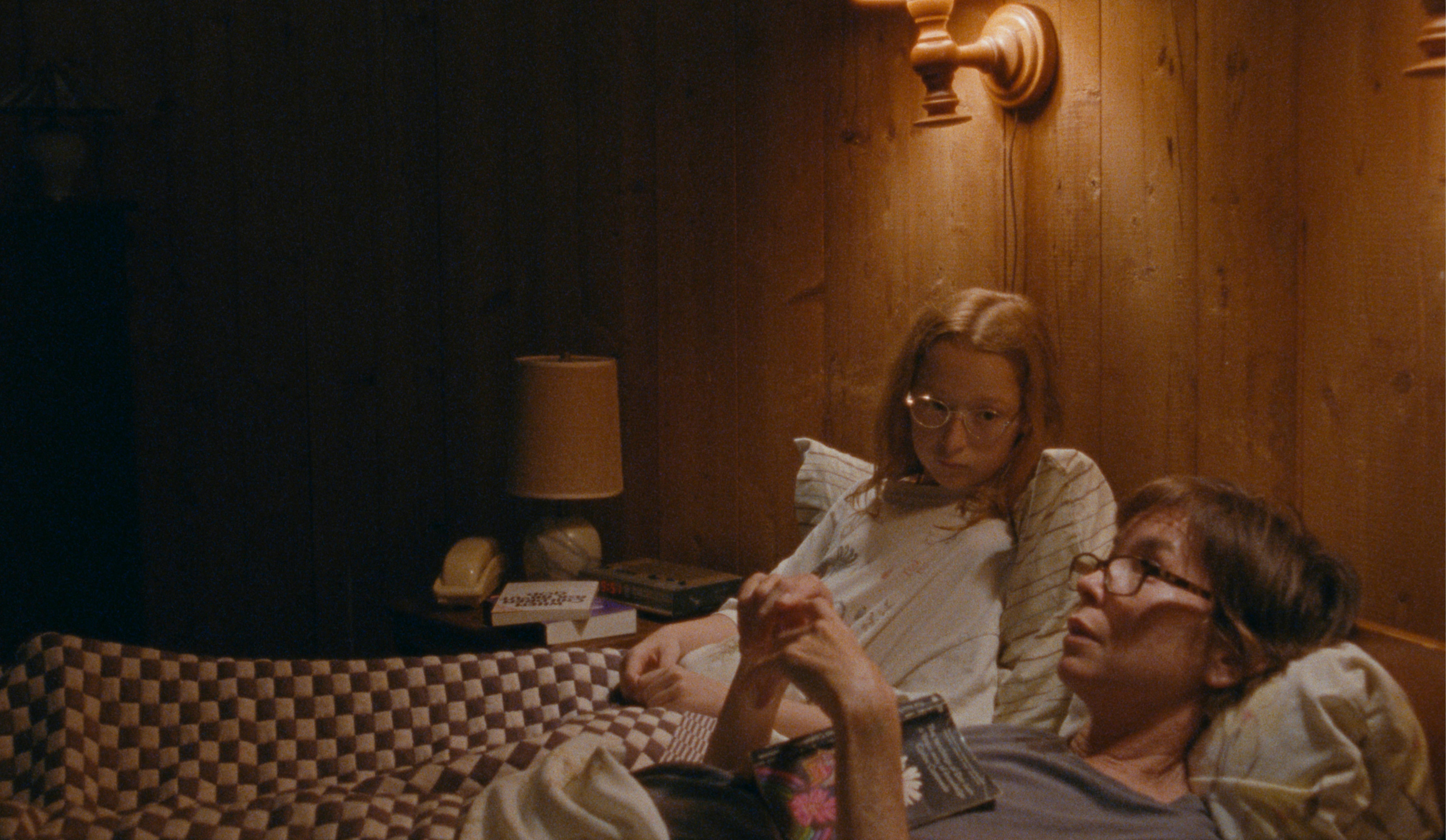 Zoe Siegler and Julianne Nicholson lying down in bed in a wood paneled room in Annie Baker’s film Janet Planet