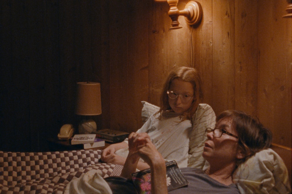 Zoe Siegler and Julianne Nicholson lying down in bed in a wood paneled room in Annie Baker’s film Janet Planet