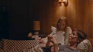 Zoe Siegler and Julianne Nicholson lying down in bed in a wood paneled room in Annie Baker’s film Janet Planet