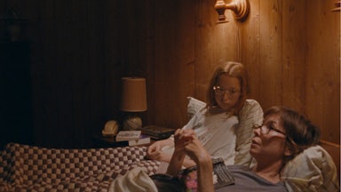 Zoe Siegler and Julianne Nicholson lying down in bed in a wood paneled room in Annie Baker’s film Janet Planet