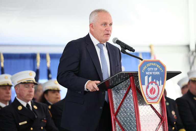 FDNY Fire Commissioner Robert Tucker speaks on stage behind a lectern that reads "Fire Department City of New York," while others speak behind him.