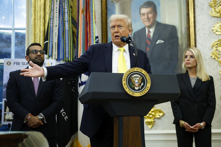 Donald Trump speaks at the presidential podium in the Oval Office while Attorney General Pam Bondi and FBI Director Kash Patel flank him on both sides and listen.