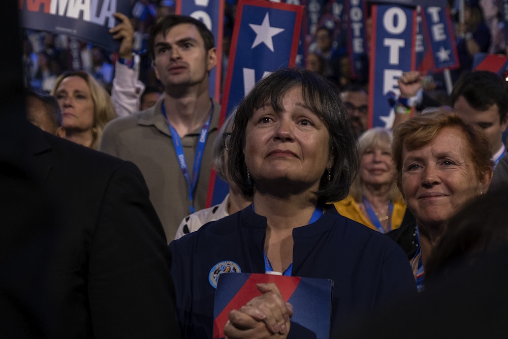 A women stands with her hands clasped in front of a crowd of onlookers watching former First Lady Michelle Obama deliver a speech on night two of the 2024 Democratic National Convention.