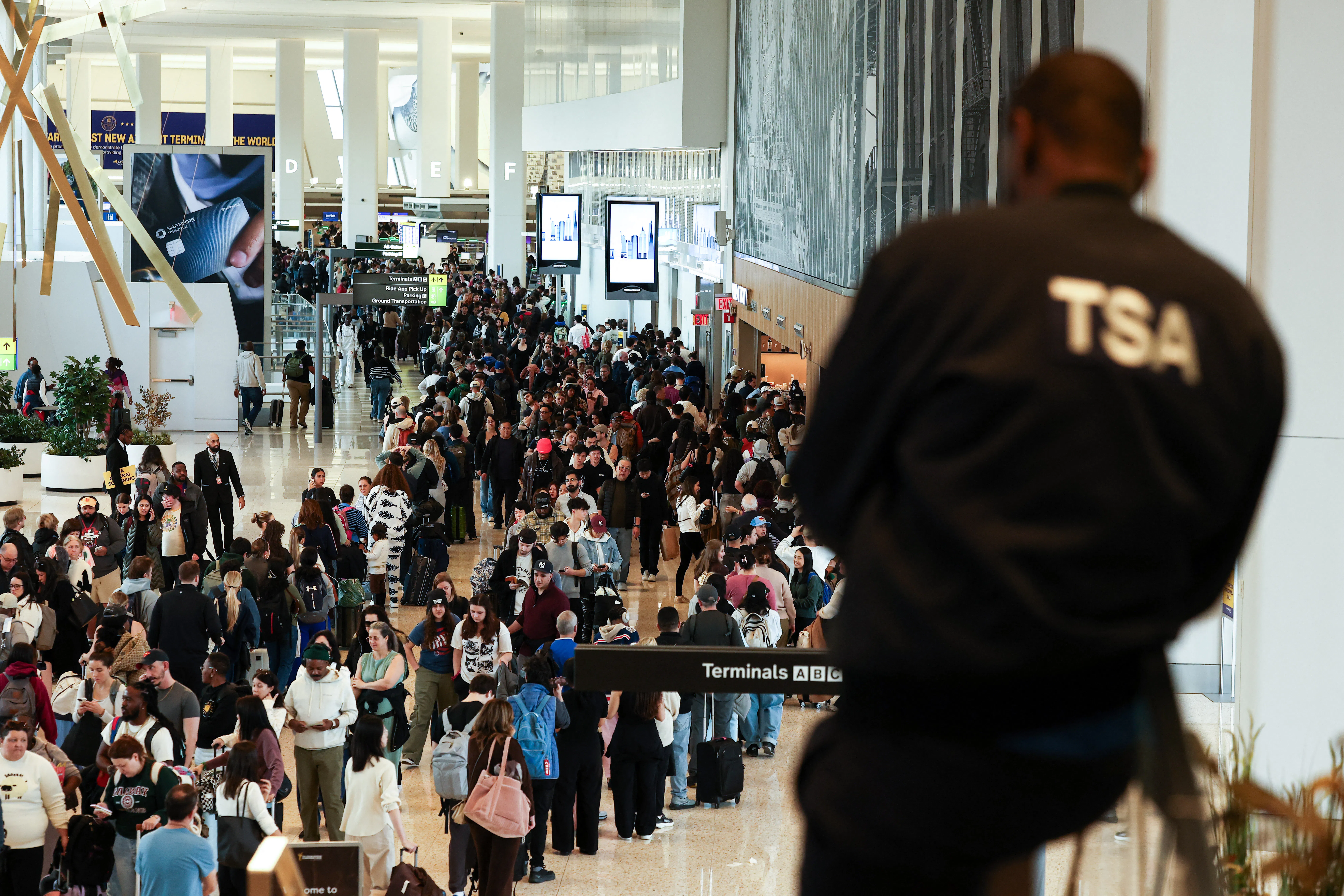 A TSA agent looks on at a massive crowd of people in the airport.
