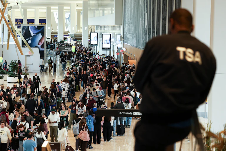 A TSA agent looks on at a massive crowd of people in the airport.