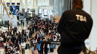 A TSA agent looks on at a massive crowd of people in the airport.