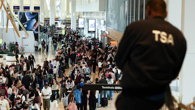 A TSA agent looks on at a massive crowd of people in the airport.