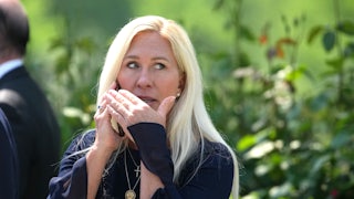 Representative Marjorie Taylor Greene puts her hand over her mouth while she speaks on the phone outdoors.