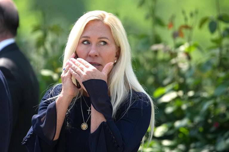 Representative Marjorie Taylor Greene puts her hand over her mouth while she speaks on the phone outdoors.