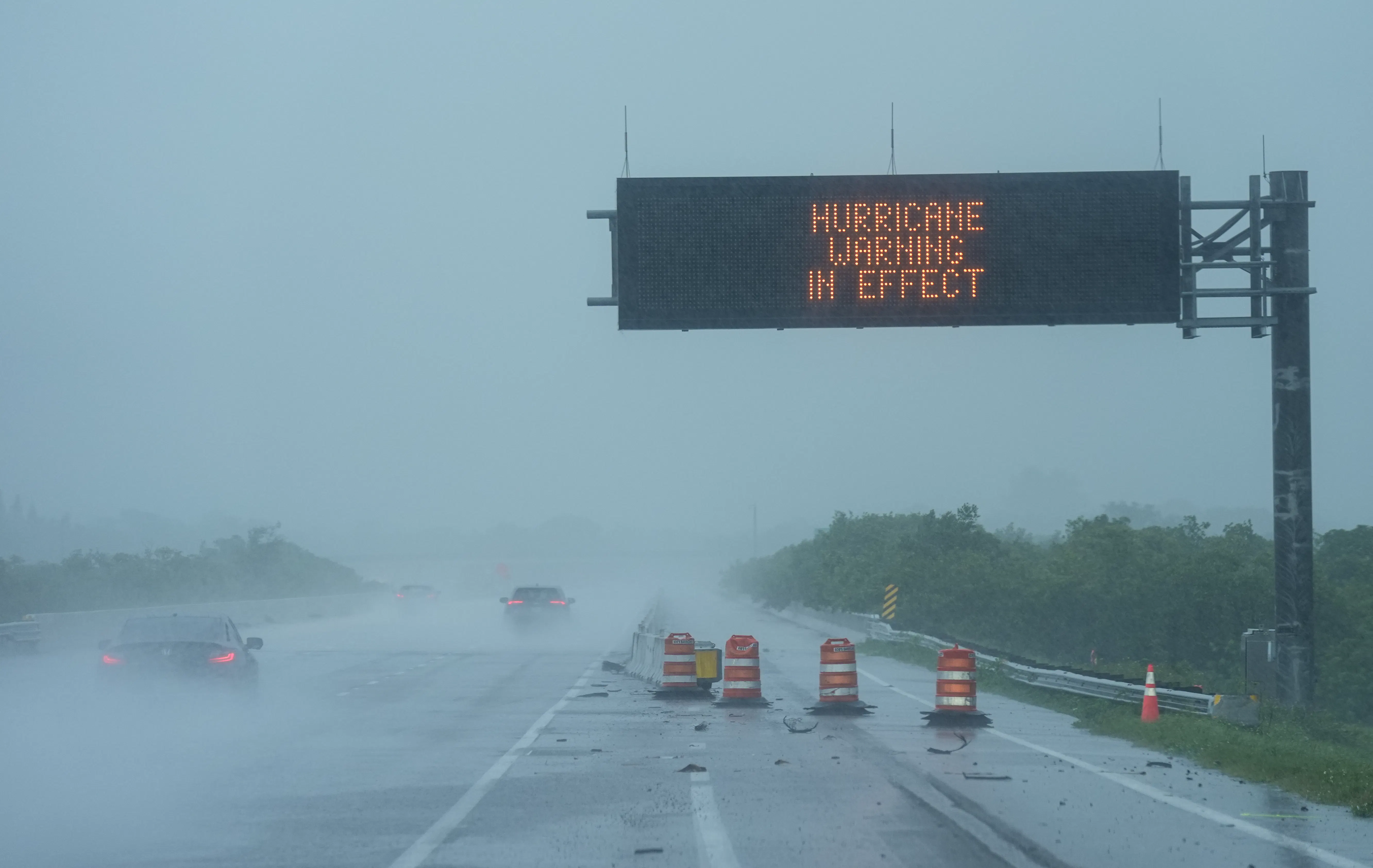 Cars drive under a road sign that says "Hurricane warning in effect" during Hurricane Milton
