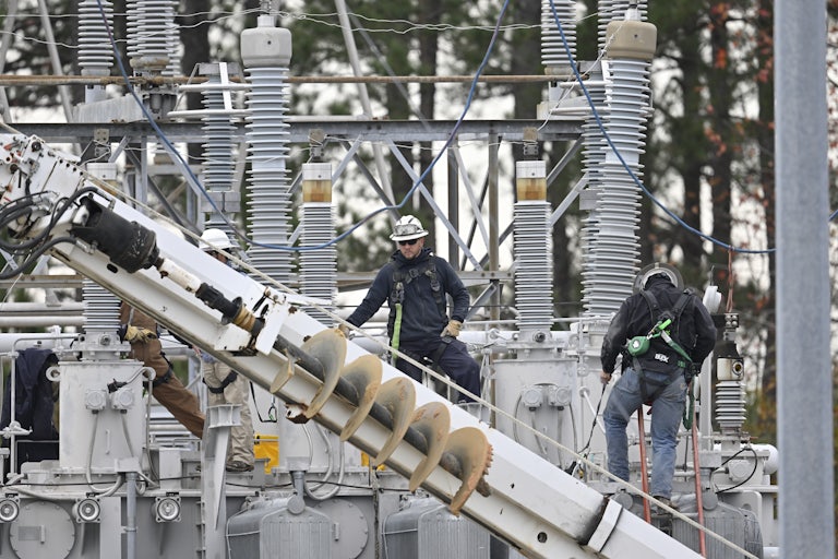 Two men in hard hats and a bunch of pipe/electric infrastructure looking things