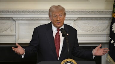Donald Trump holds his arms out to the side while speaking at a podium