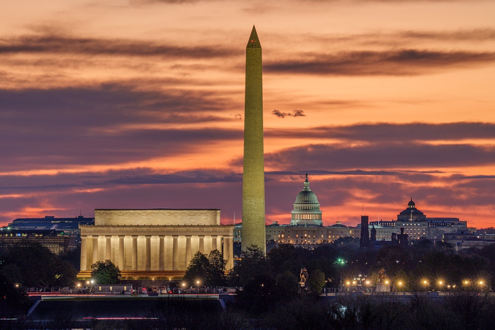 Sunrise turns the sky shades of orange behind the Lincoln Memorial, Washington Monument, and U.S. Capitol Building in Washington, D.C.
