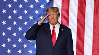 Donald Trump salutes while standing in front of a massive American flag