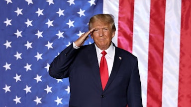 Donald Trump salutes while standing in front of a massive American flag