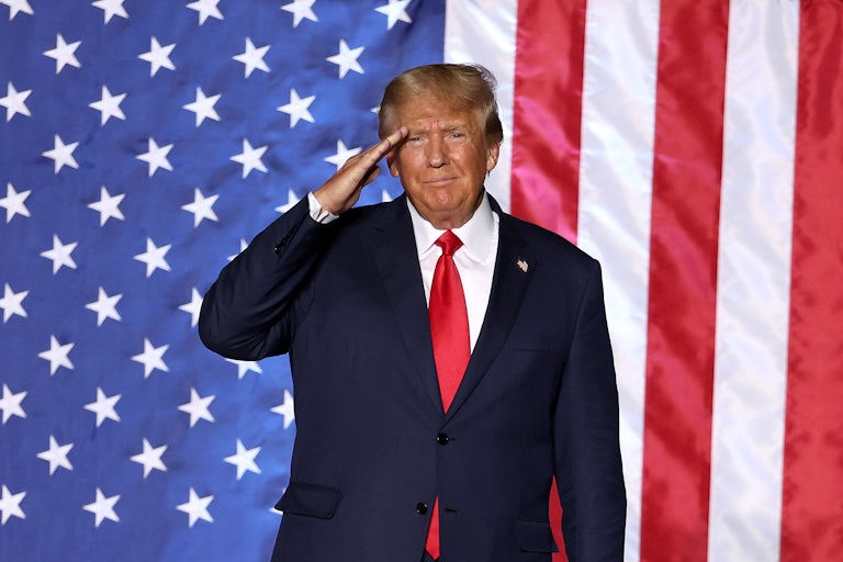 Donald Trump salutes while standing in front of a massive American flag