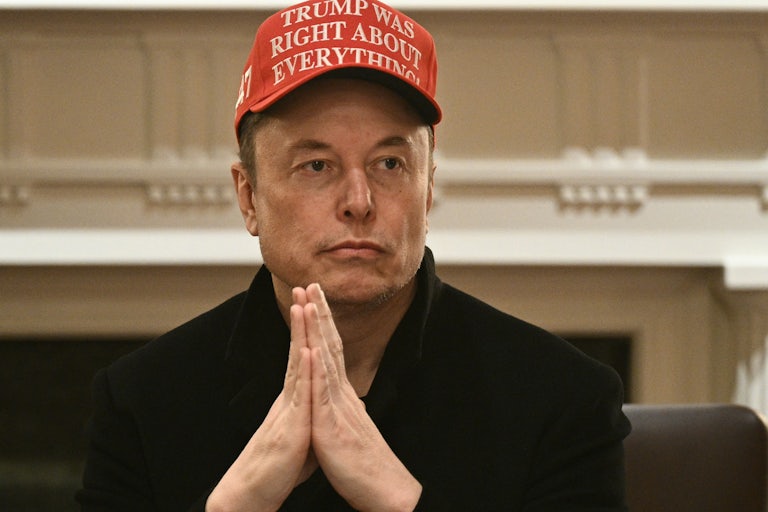 Elon Musk puts his hands together as if in prayer and wears a red cap reading "Trump was right about everything."
