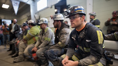 Coal miners sit in a room on chairs waiting.