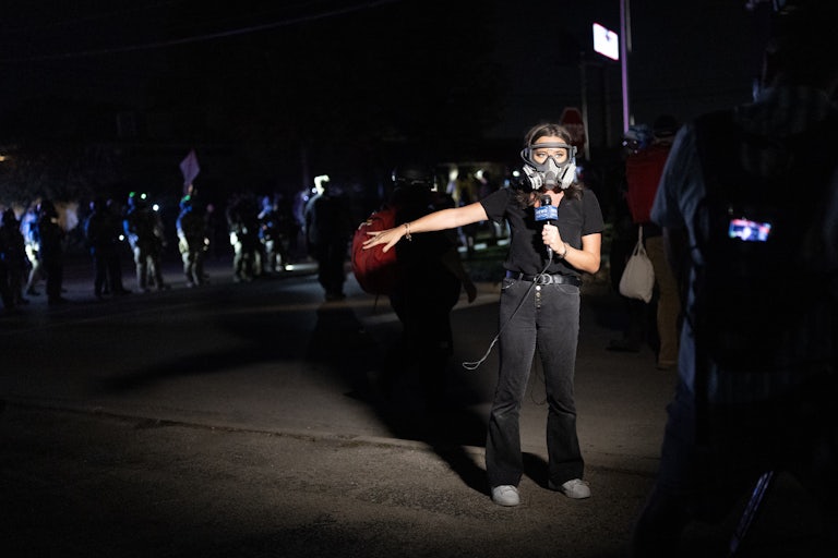 A television journalist wears a gas mask and reports from a demonstration outside of an immigration processing center in Broadview, Illinois
