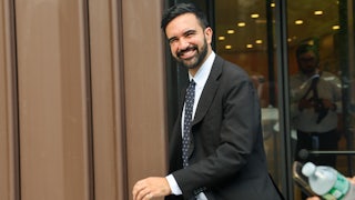 Zohran Mamdani smiles while walking out of a building