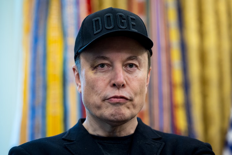 Elon Musk wears a black DOGE cap and purses his lips. He is sporting a black eye.