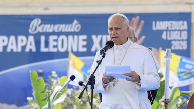 Pope Leo holds a stack of papers and speaks into a microphone
