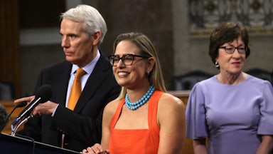 Arizona Senator Kyrsten Sinema smiles as she stands between Senator Rob Portman and Senator Susan Collins.