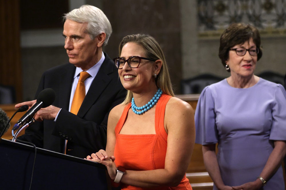 Arizona Senator Kyrsten Sinema smiles as she stands between Senator Rob Portman and Senator Susan Collins.