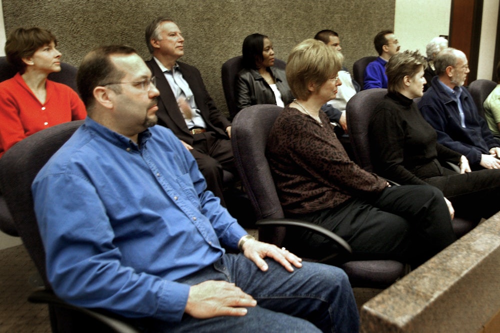 Twelve jurors sit in the jury box, listening attentively.
